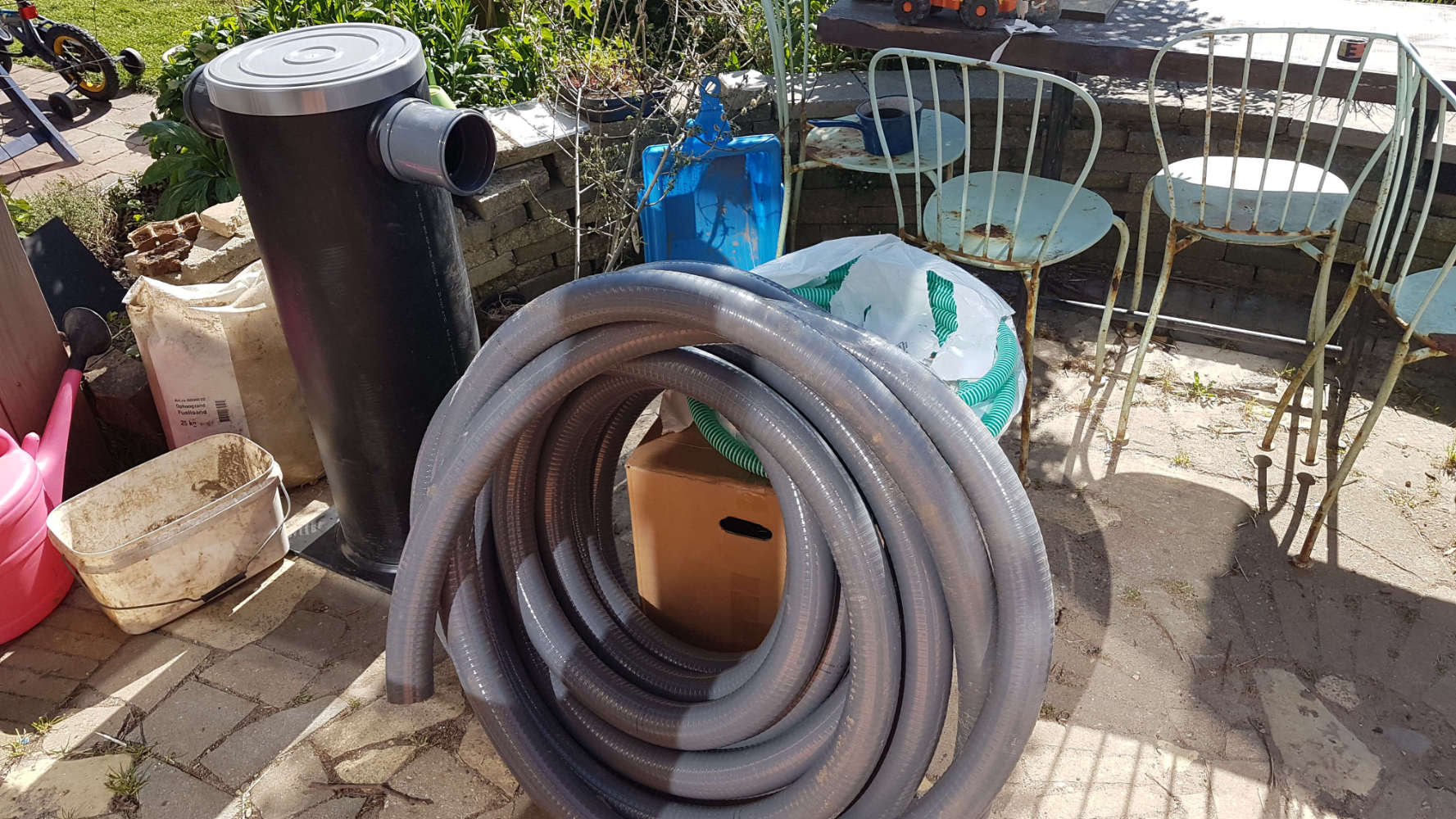 Filterput (met daarin filter en vlotter) en aansluitmateriaal in de tuin voor installatie